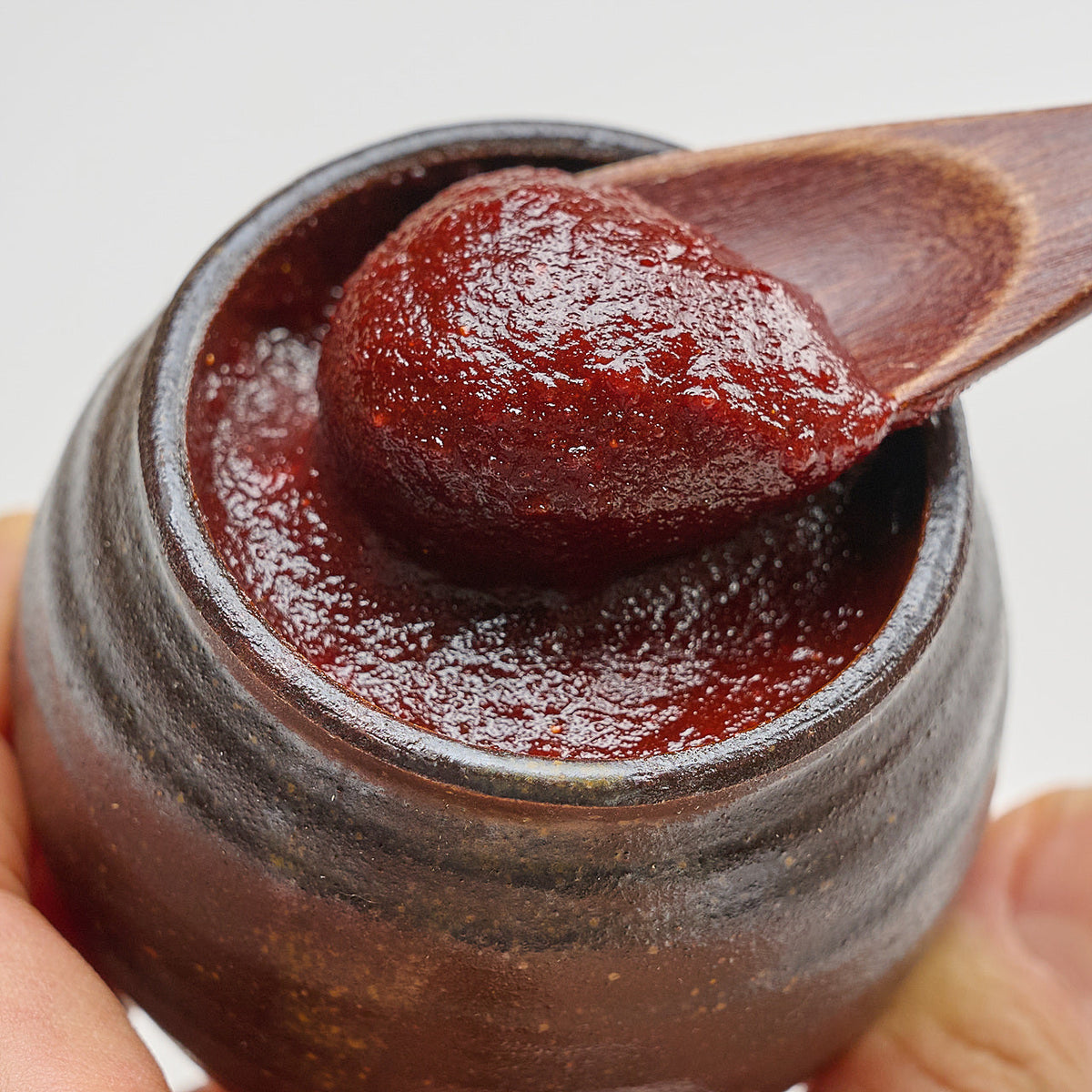 Gochujang in a ceramic jar lifted with a wooden spoon