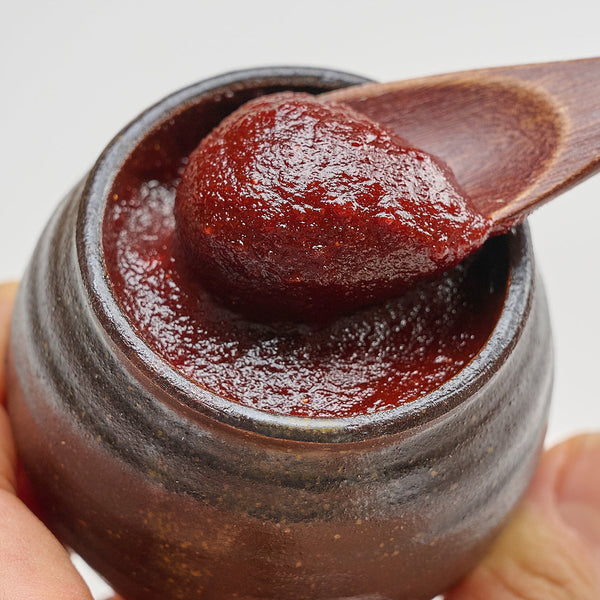 Gochujang in a ceramic jar lifted with a wooden spoon