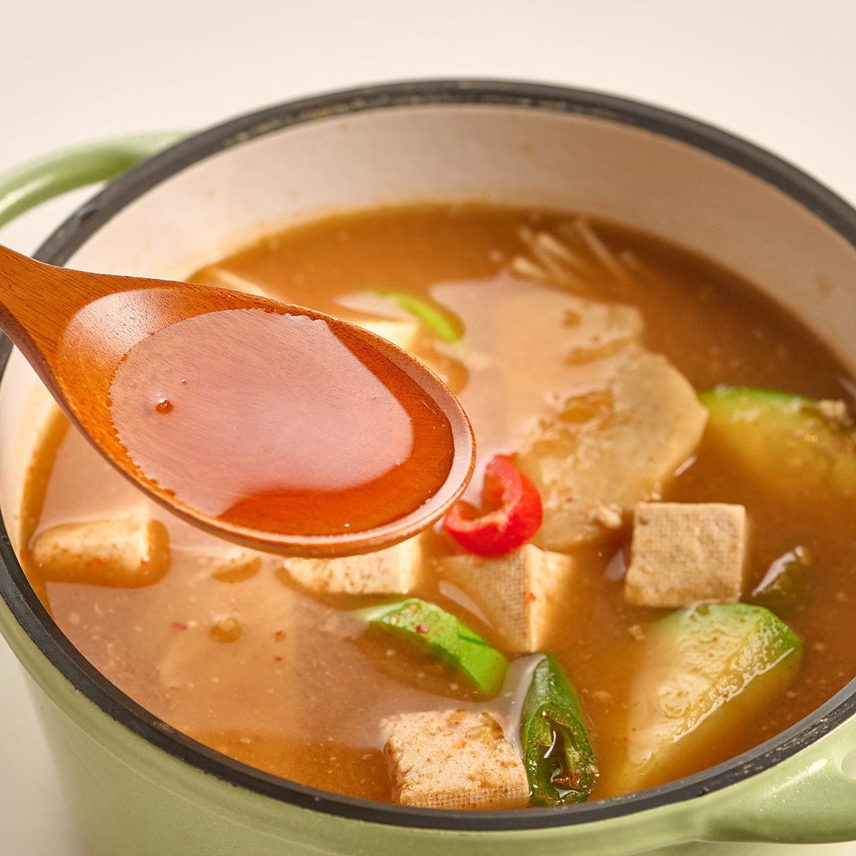 Spoonful of broth lifted from a pot of doenjang soup with tofu and zucchini